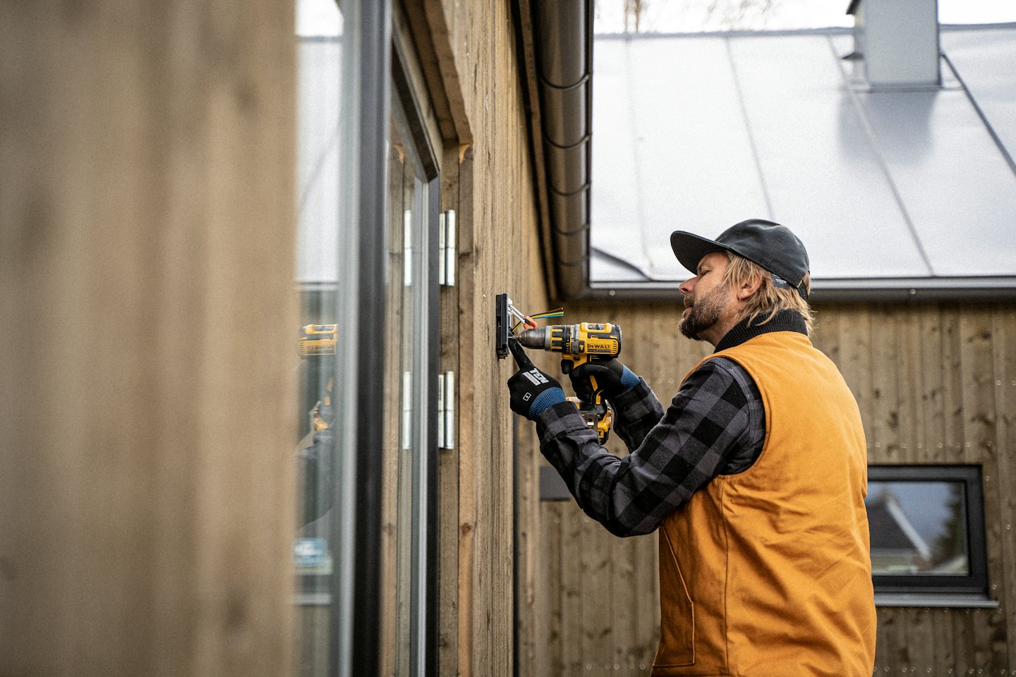 Man in plaid shirt installs siding with power drill.